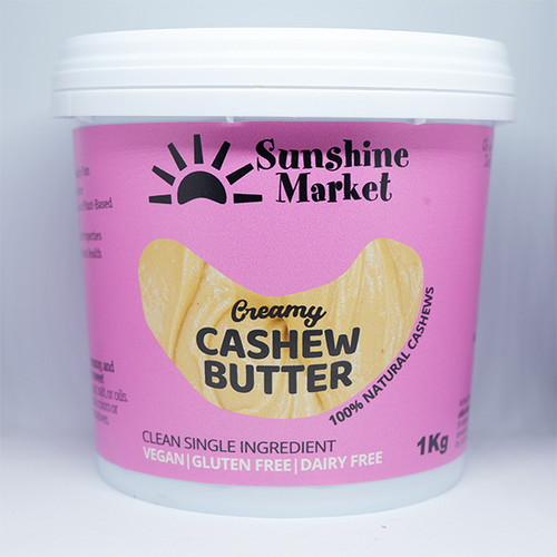 A container of Sunshine Market Cashew Butter, 1kg size, with a pink label indicating that it's creamy, natural, vegan, gluten-free, and dairy-free.